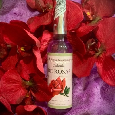 Frasco de colónia de rosas rodeado por pétalas vermelhas sobre pano lilás