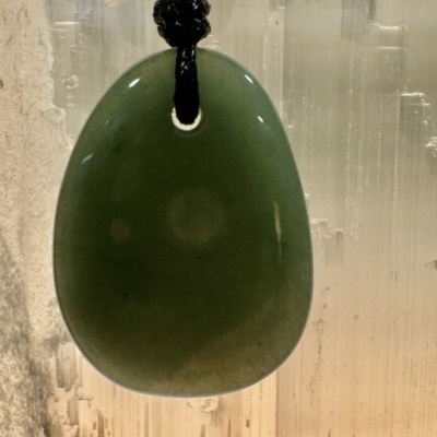 Pendente verde polido com cordão preto suspenso em fundo translúcido