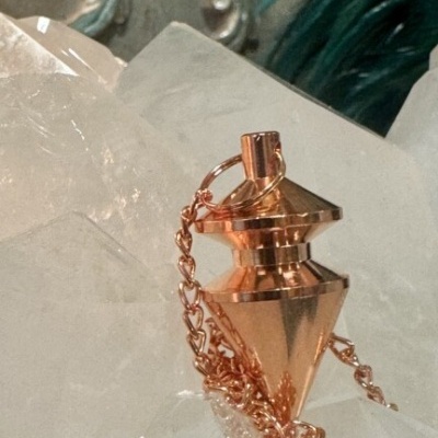 Pêndulo de metal cor de cobre com correntes sobre base de cristal transparente