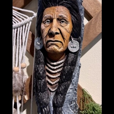 Escultura de rosto indígena detalhado em madeira com colares e brincos grandes