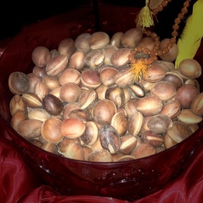 Recipiente transparente com sementes marrons e colar de contas sobre tecido vermelho