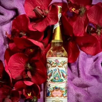 Frasco de bebida Agua de Florida entre flores vermelhas num tecido roxo