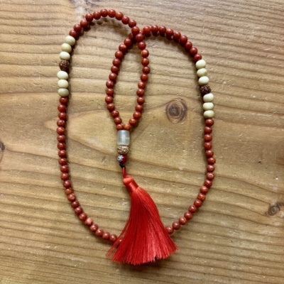 Colar ou mala de contas vermelhas e brancas com tassel vermelho sobre madeira clara
