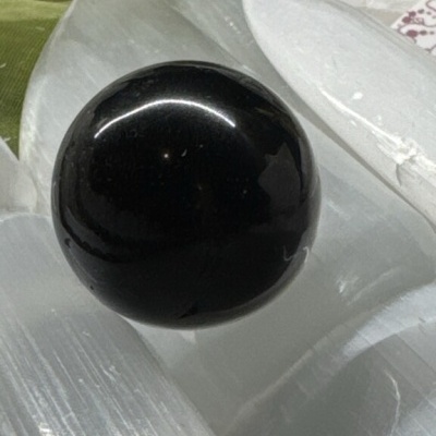 Esfera preta brilhante sobre lâminas claras em fundo com tecido verde e prato branco