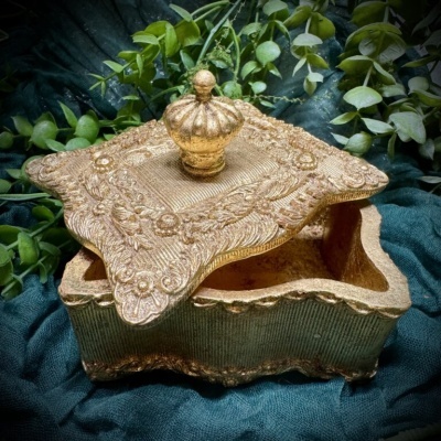 Caixa decorativa dourada com tampa ornamentada e botão em forma de coroa