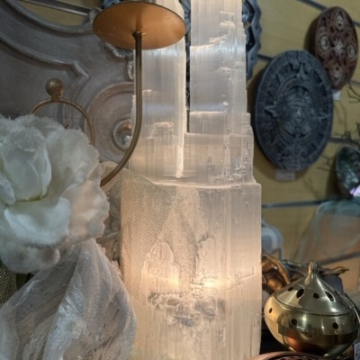 Escultura de cristal translúcido em formato de torre com tecido branco e objetos decorativos ao redor, parede amarela ao fundo