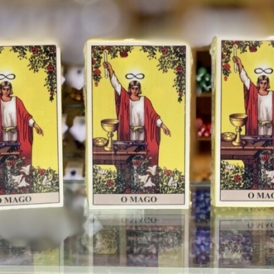 Cinco baralhos de tarot Rider Waite alinhados sobre superfície espelhada com a carta O MAGO na frente.