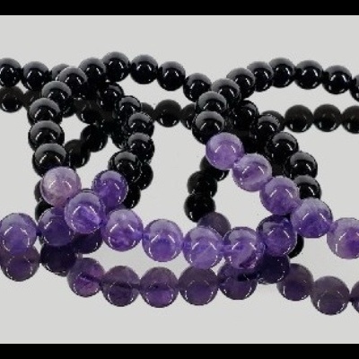 Três pulseiras de contas pretas e roxas em fundo cinza claro