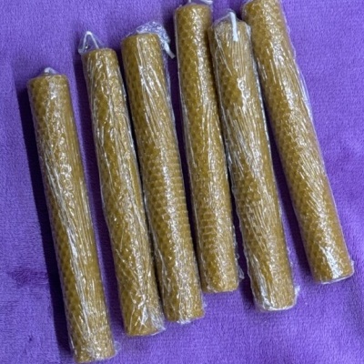 Seis velas de cera de abelha enroladas em padrão de favo hexagonal sobre tecido roxo.