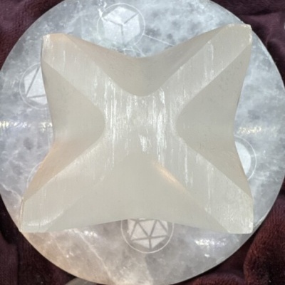 Escultura geométrica em cristal branco sobre base circular com símbolos, em fundo de tecido bordô