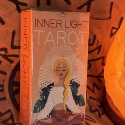 Caixa de tarot Inner Light com ilustração de mulher meditativa e fundo com símbolos