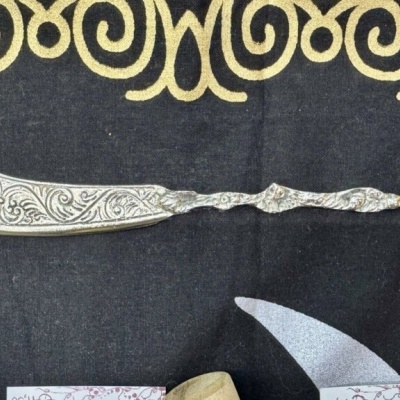 Navalha metálica decorativa com cabo e lâmina gravados sobre tecido preto com padrão amarelo