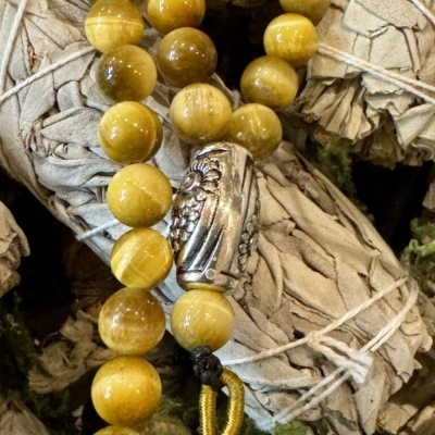 Colar ou pulseira com contas amarelas e detalhe metálico prateado sobre folhas secas