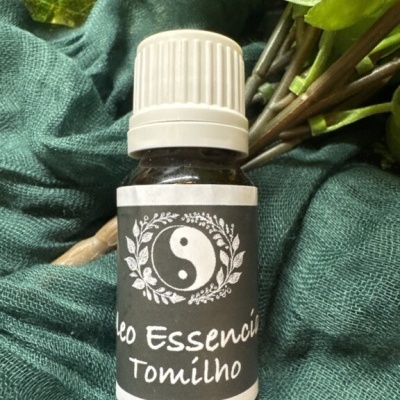 Frasco de óleo essencial de tomilho com rótulo preto e tampa branca sobre tecido verde