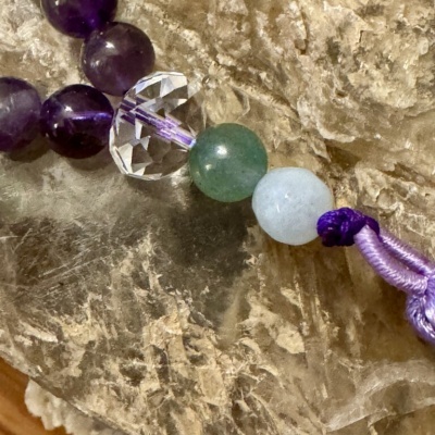 Pulseira com contas coloridas e cordão roxo sobre pedra texturizada