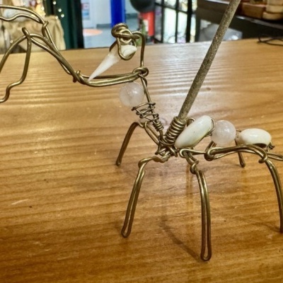 Escultura de insecto em arame dourado com bolas brancas e transparente numa mesa de madeira