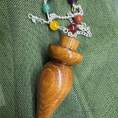 Pingente de madeira com corrente e contas coloridas sobre tecido verde