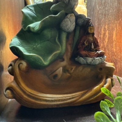 Escultura decorativa com figura sentada e folhas verdes em base castanha