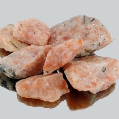 Pedras minerais rosas alaranjadas com textura rugosa em superfície reflexiva cinza.