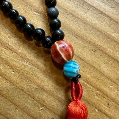 Colar com contas pretas, vermelha, azul e tassel vermelho sobre madeira