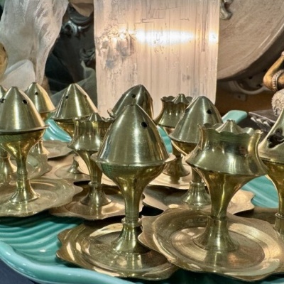 Incensários de latão dourado sobre prato verde água com estátua de Ganesha ao fundo