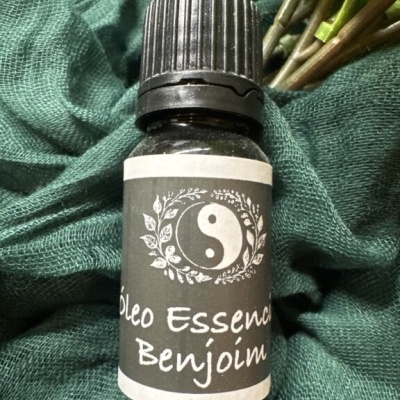 Frasco de óleo essencial de benjoim com rótulo preto e tampa preta sobre tecido verde
