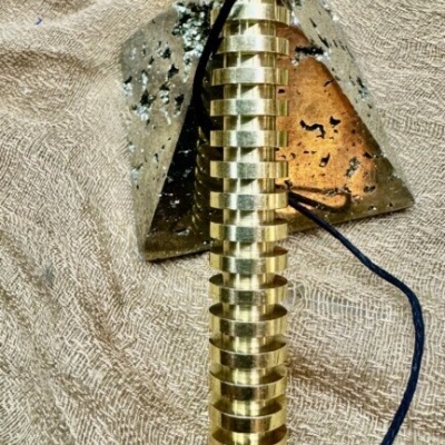 Pêndulo dourado espiral metálico com cabo preto sobre tecido bege com pirâmides de vidro