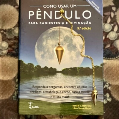 Livro sobre radiestesia com pêndulo dourado posicionado em cima.