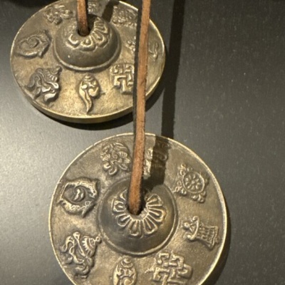 Dois pequenos címbalos de metal com padrões gravados e cordão de couro