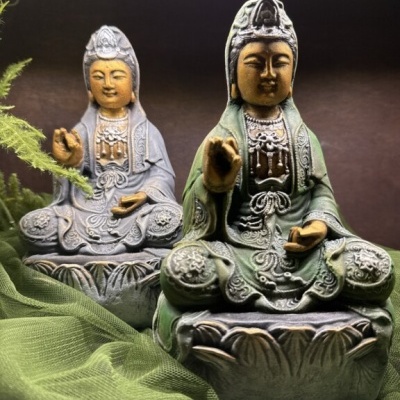 Duas estátuas ornamentadas de figura sentada, verde e cinza, com tecido verde