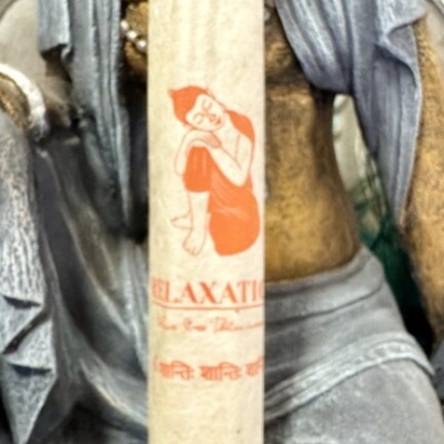 Incenso com embalagem branca e ilustração laranja junto a estátua cinzenta