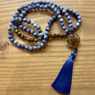Colar ou pulseira de contas azuis, marrons com pendente redondo e tassel azul sobre madeira
