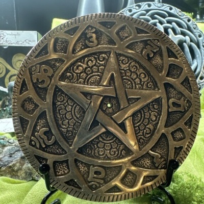 Placa decorativa metálica com pentagrama e símbolos em suporte preto sobre tecido verde