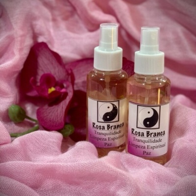 Dois frascos de spray com rótulos Rosa Branca sobre tecido rosa e uma flor