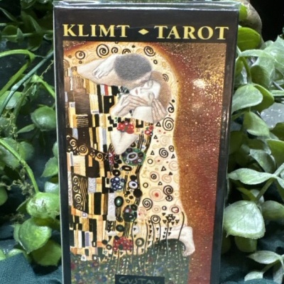 Caixa do baralho de tarot Klimt Tarot com arte dourada e preta inspirada em Gustav Klimt, num fundo de plantas verdes.