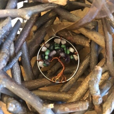 Pingente redondo com árvore de fio de cobre e pedras coloridas dentro de ramos de madeira.