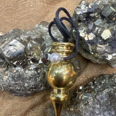 Pingente dourado com cordão preto sobre pedras metálicas
