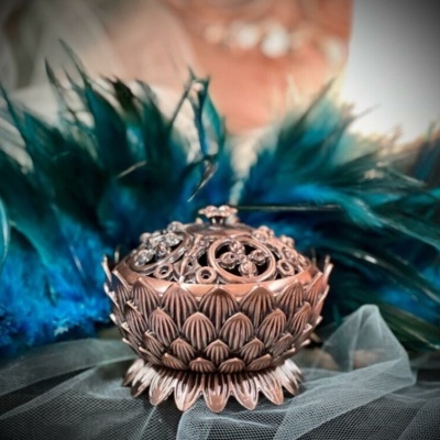 Incensário de metal cobre com padrão de pétalas e tampa decorativa em tecido de tule cinza e penas azuis