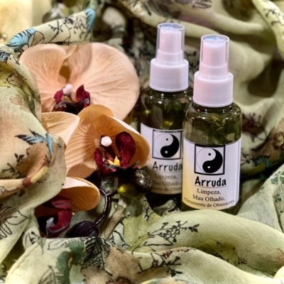 Duas garrafas de spray Arruda sobre tecido floral com flores artificiais