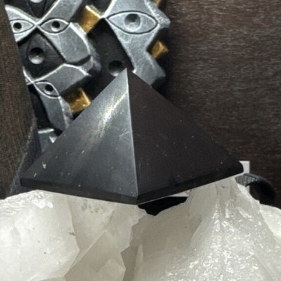 Pirâmide preta sobre cristal branco com objeto metálico ao fundo