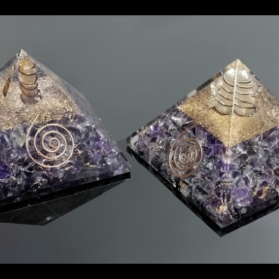 Duas pirâmides de orgonite com detalhes em cobre e base roxa sobre superfície preta