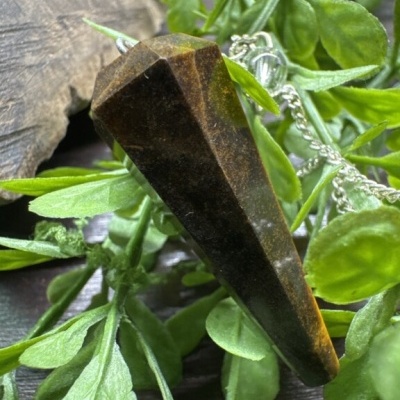 Pêndulo de cristal marrom facetado com corrente azul entre folhas verdes e madeira.