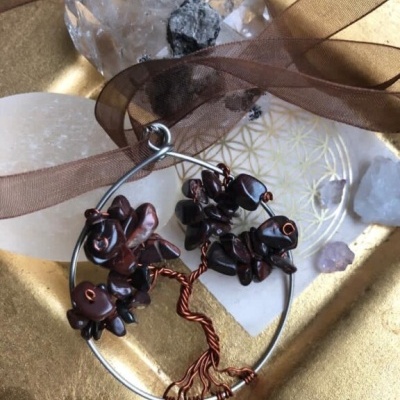 Anel em forma de árvore com fios de cobre e pedras castanhas num prato dourado com pedras translúcidas