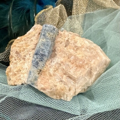 Roca mineral rosada com faixa cinzento-azulada sobre tecido de malha verde e dourado.
