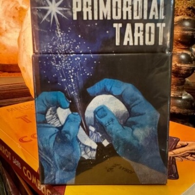Caixa do baralho PRIMORDIAL TAROT com ilustração de mãos azuis segurando cristais