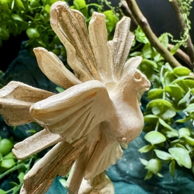 Estátua decorativa pássaro cerâmico bege dourado com plantas verdes ao fundo