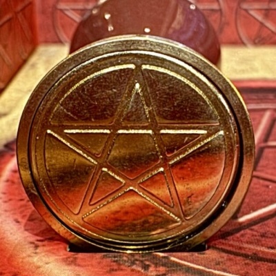 Objeto cilíndrico dourado com pentagrama sobre pano vermelho com padrões.