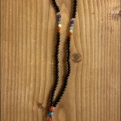 Colar de contas pretas com contas coloridas e tassel vermelho em fundo de madeira.