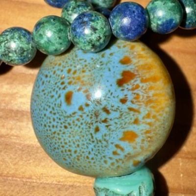 Colar com contas em tons de azul, verde e castanho sobre mesa de madeira