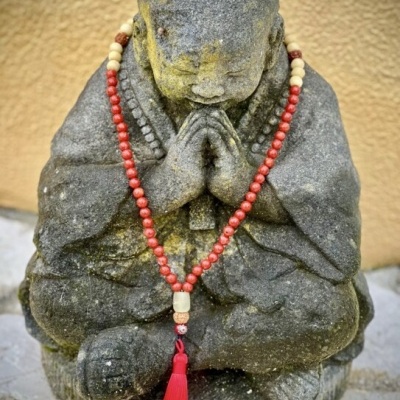 Estátua de monge de pedra com contas vermelhas e bege e borla vermelha